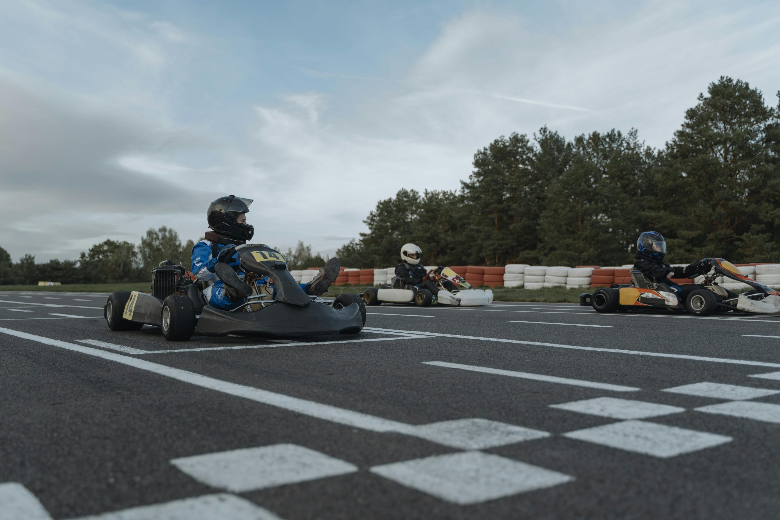 Three racers in go-karts compete on an outdoor track starting line.